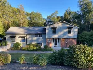 Split-level home with new gray vinyl siding, landscaping in front.