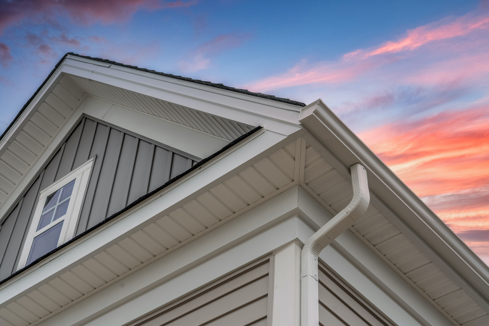 Angled view of home's exterior siding and gutters with sunset in the background.