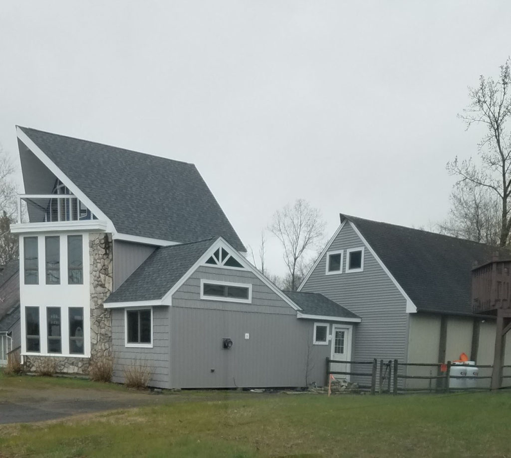 Two story house with angled roof, new windows, and attached garage with grey siding