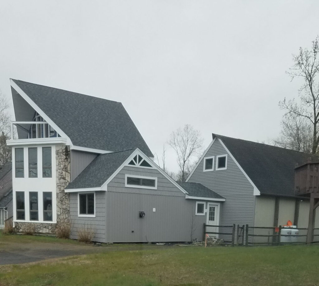 Two story house with angled roof, new windows, and attached garage with grey siding