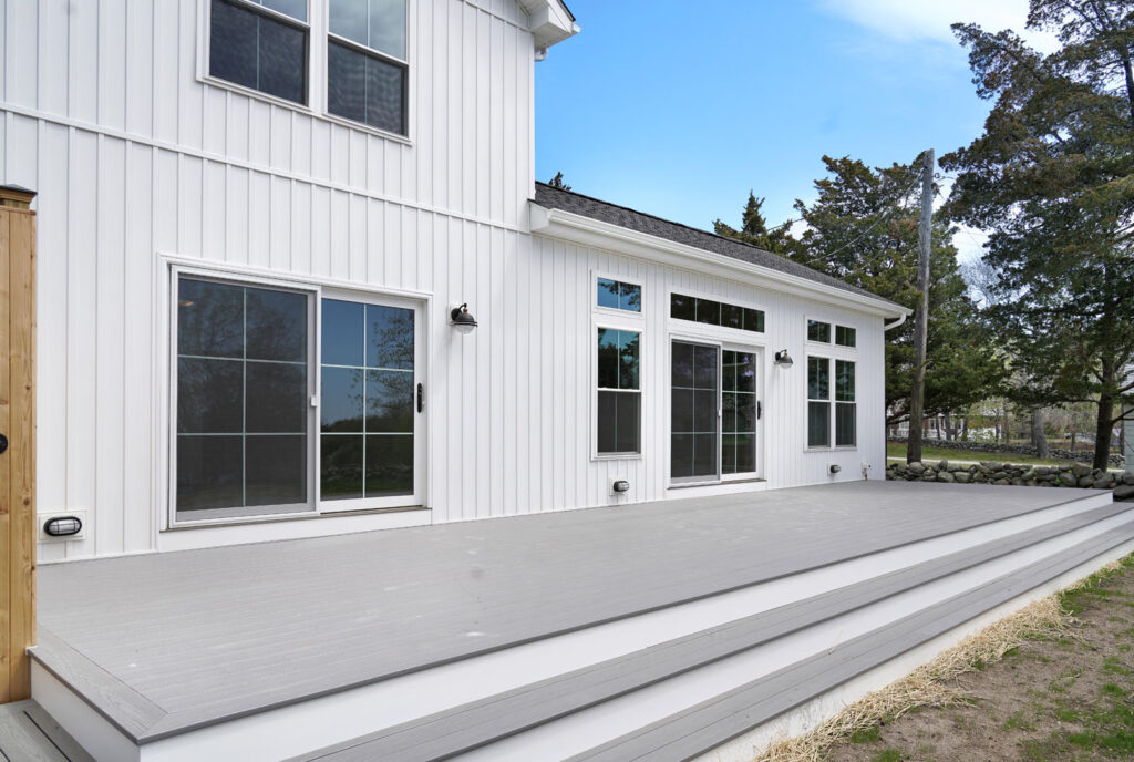 Back of white house with new vertical siding, windows, and attached deck