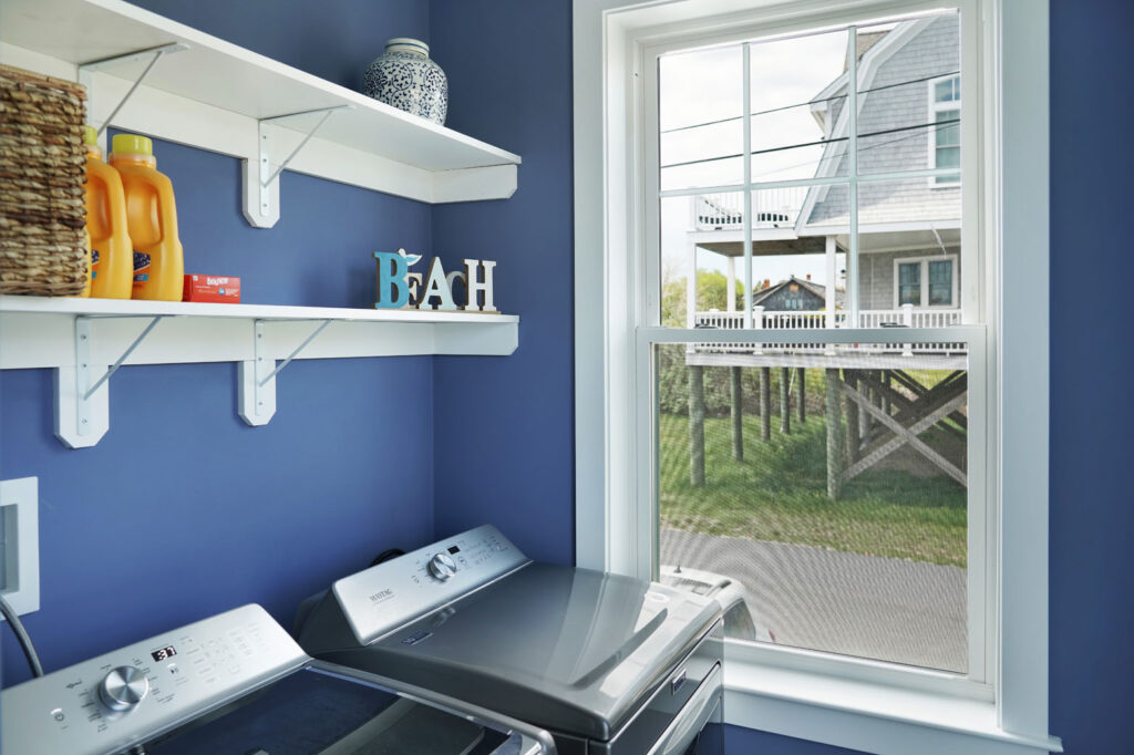 Laundry room with blue painted walls and new stainless steel washer and dryer and window with view of neighbors house