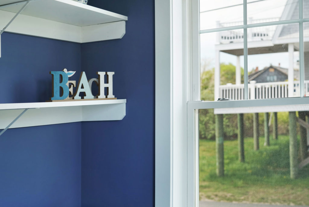White shelving in laundry room with blue painted walls and window with white trim and beach decoration