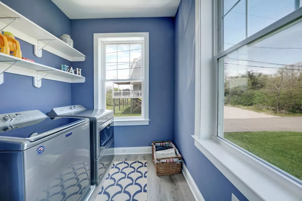 A laundry room with blue painted walls, gray wooden flooring, and built-in shelving.