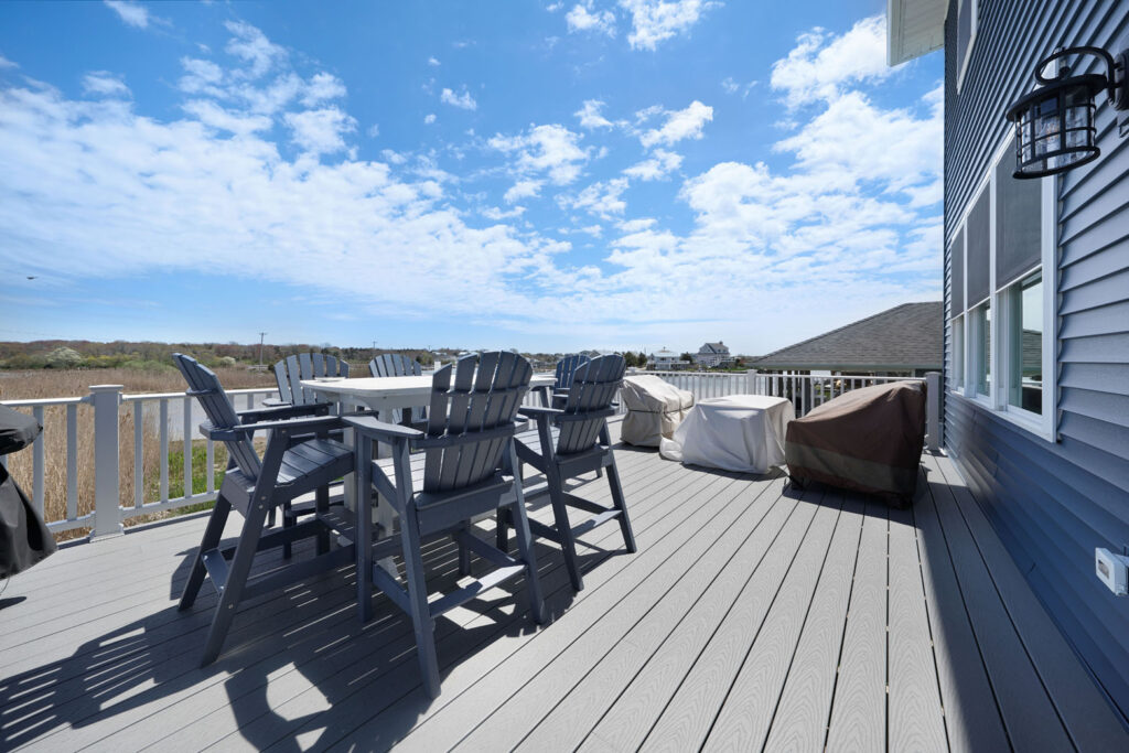 A gray painted back porch with a matching pub-height picnic table and adirondack chairs.