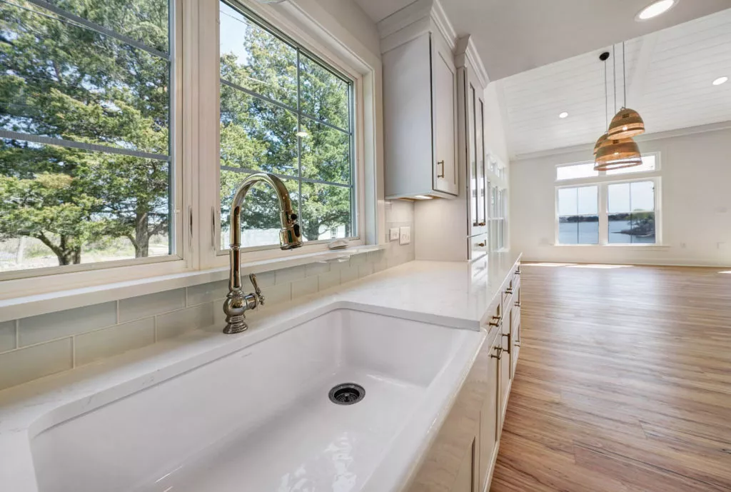 A modern kitchen with white marble counters, white cabinets, and light wooden flooring.