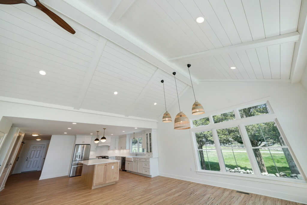 Inside a residential, two-story house's living room. A-frame ceiling qwith light fixtures hanging from the ceiling.