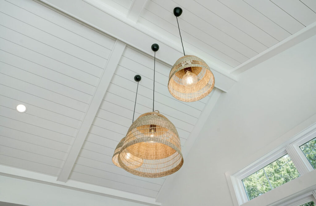 Three wooden lightfixtures hanging from white, A-frame roof.