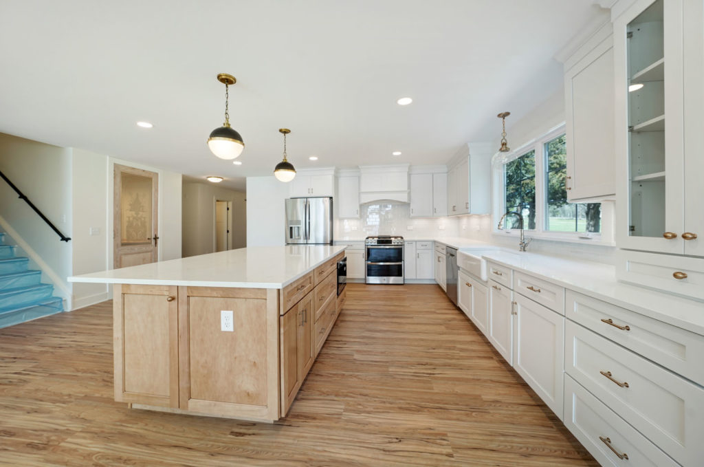 A modern kitchen with white cabinets, gold hardware, and a white marble island.