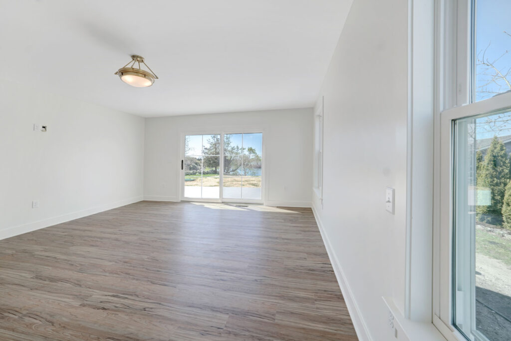 An empty room with light wooden flooring and sliding glass doors that lead onto a patio.