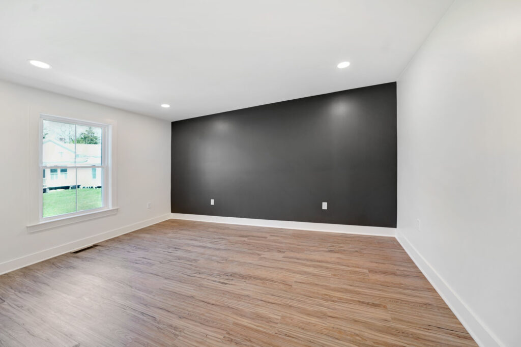 An empty bedroom with white walls, light wooden flooring, and a black accent wall.