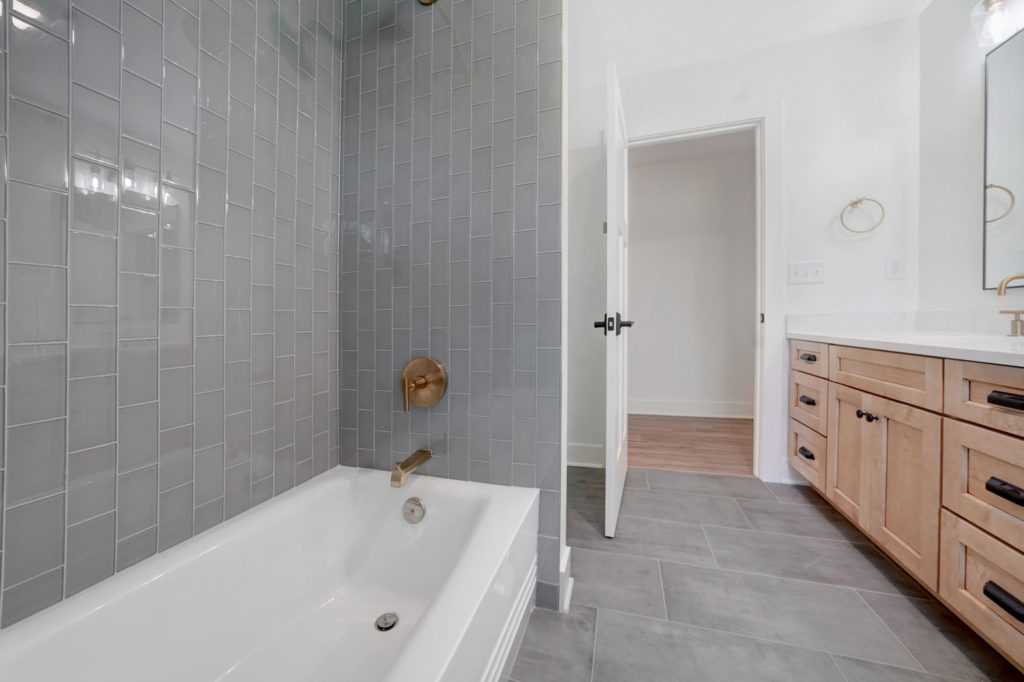 Bathroom with a tub, brass fixtures, and a grey tiled shower.