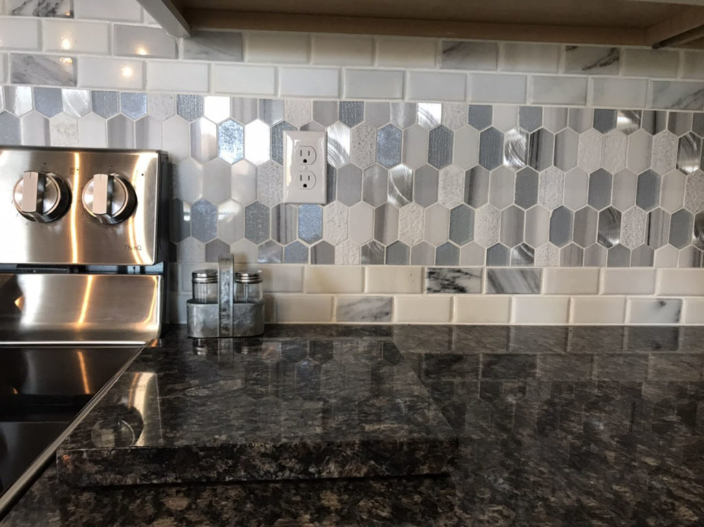 A kitchen counter with dark marble countertops and a gray and white honeycomb backsplash.