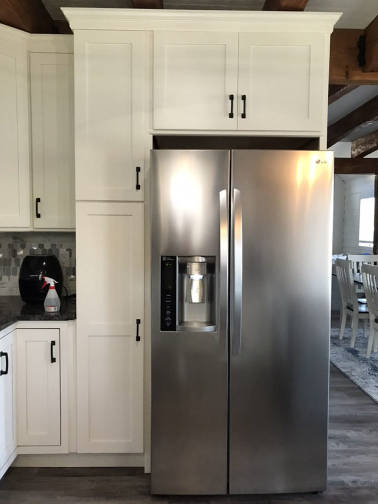 Kitchen with gray wood flooring, white cabinets, and a stainless steel fridge.