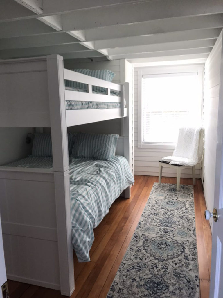 A small bedroom with dark wooden floors, white shiplap walls, and bunk beds.