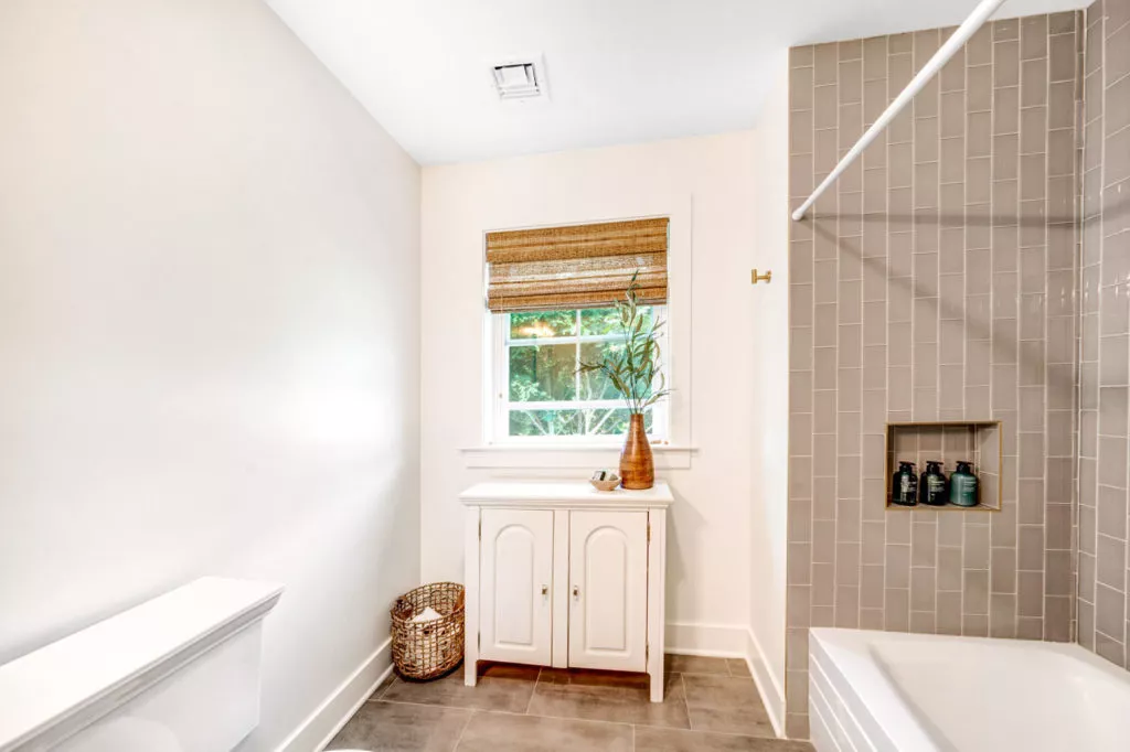 White cabinet with potted plant on it inside of residential bathroom. A bathtub can also be seen.