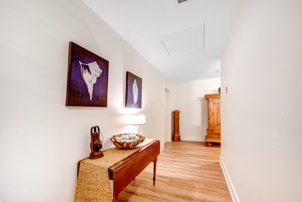 Corridor inside home with wooden floors, decorative table and purple artwork mounted on white walls.