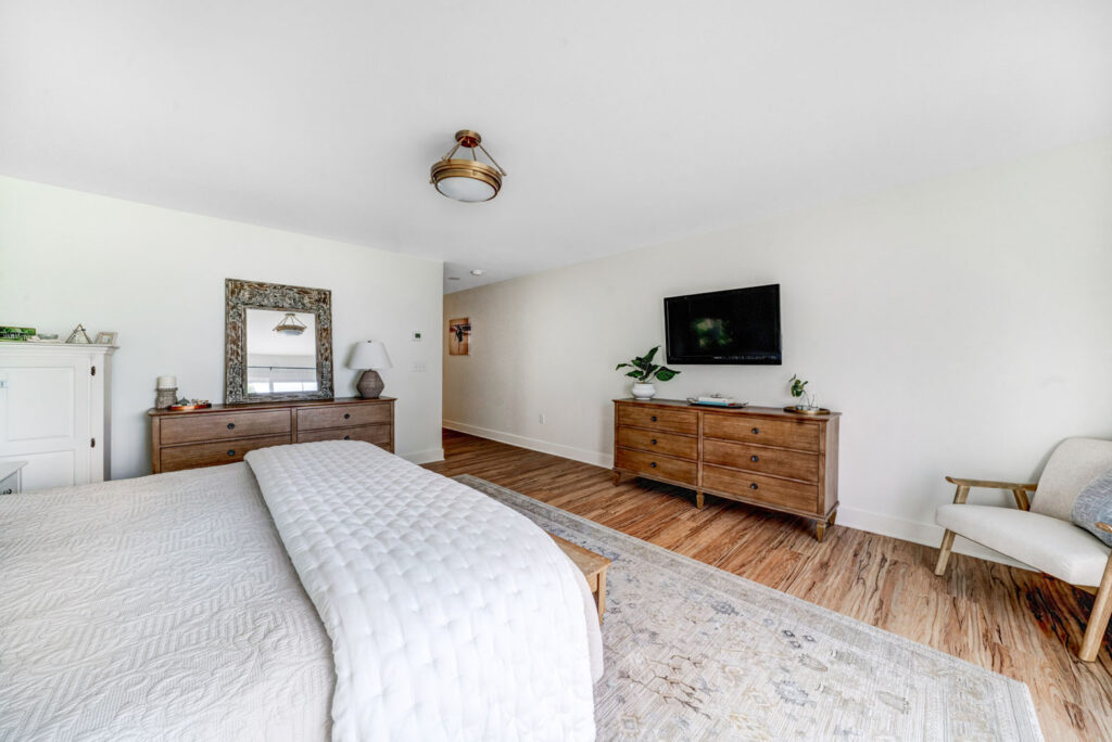 Bedroom inside home featuring a bed, cabinets, TV, mirror, rug and decorative chair.