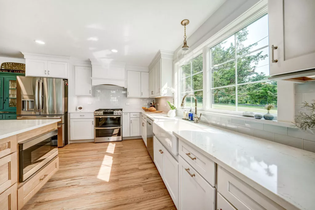 Natural daylight coming through large windows into modern, white, residential kitchen.