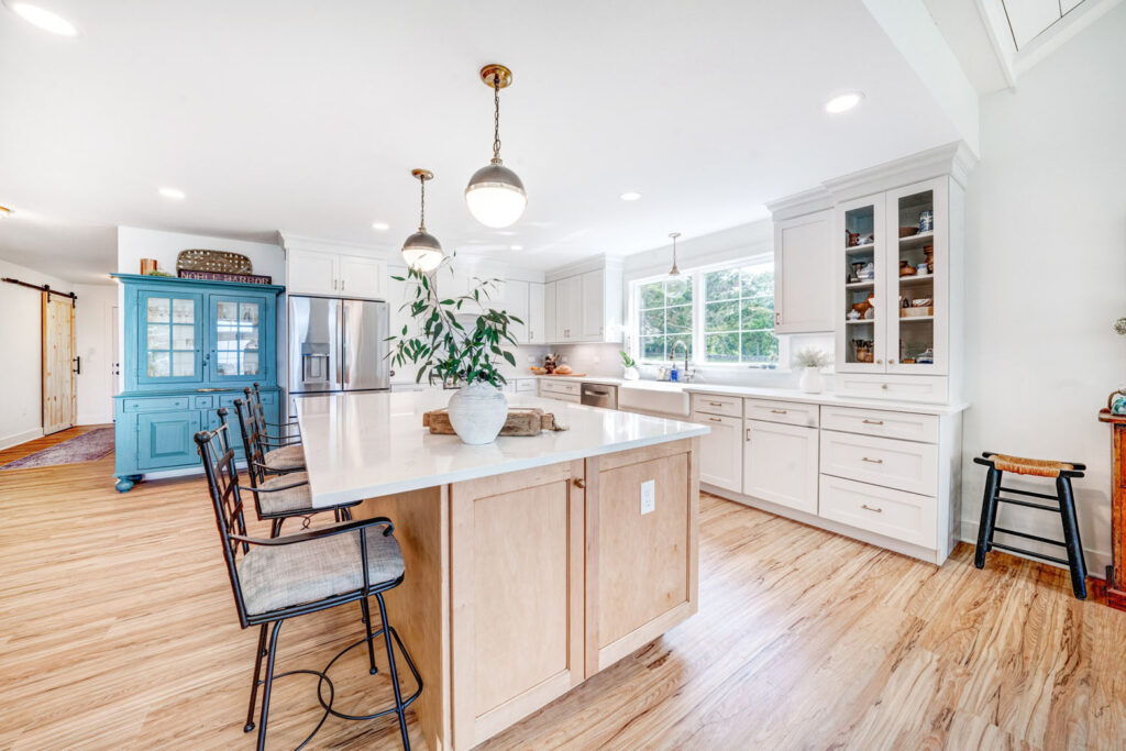 Large kitchen island with plantpot and chairs inside white, residential kitchen area.