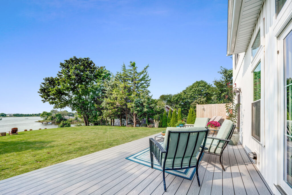 Chairs on a backyard deck overlooking grass and lake in the background.