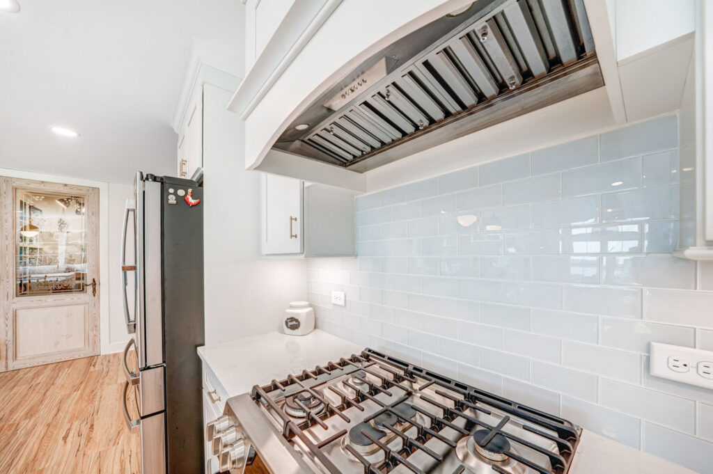 A view of a kitchen with a gas kitchen stove, white counters, and a white tile backsplash.