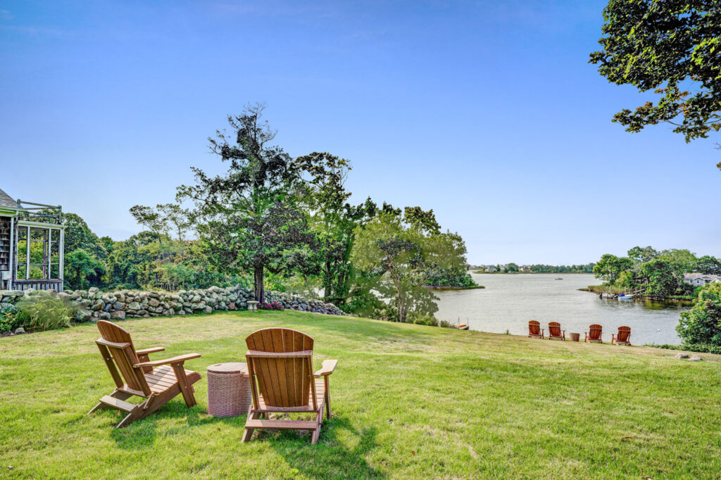 Wooden chairs in grassy backyard overlooking a lake.