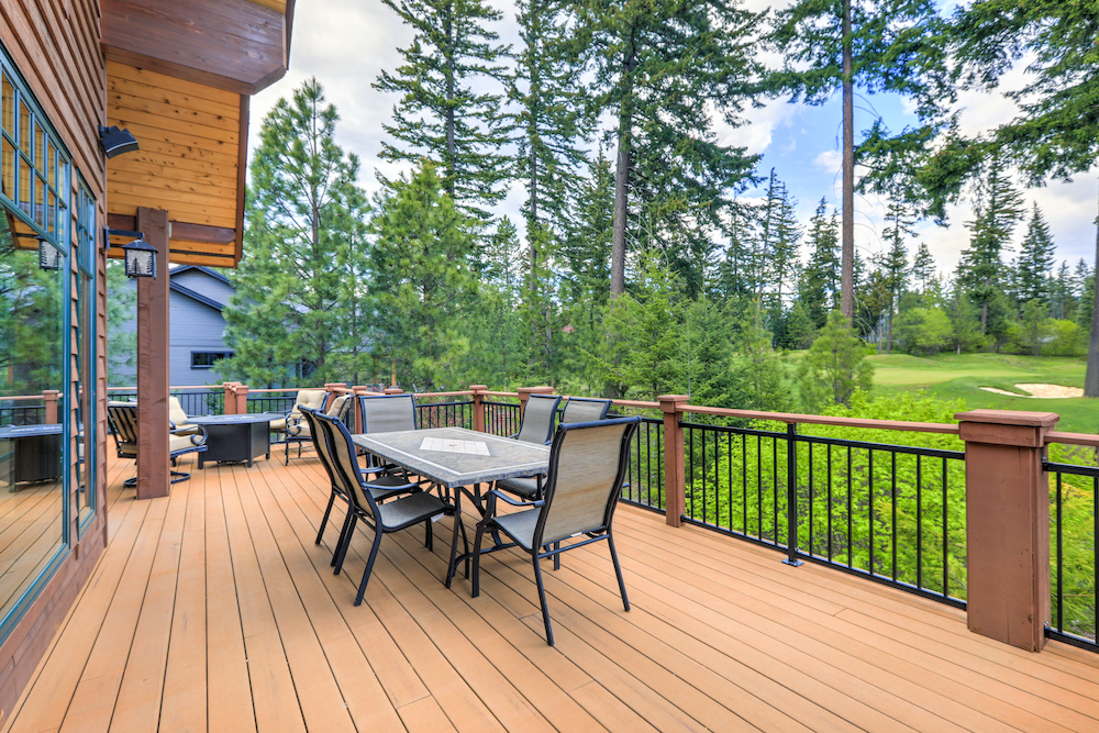 Beautiful large cabin home with large wooden deck and chairs with table overlooking golf course.