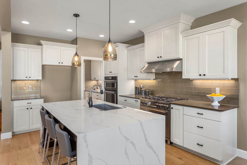 Kitchen in new luxury home with waterfall isalnd, stainless steel appliances, pendant lights, and hardwood floors