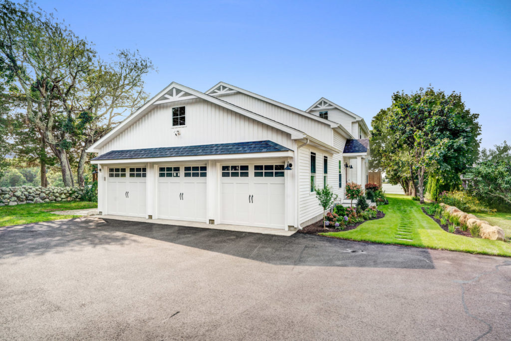 Three-car garage on side of beautiful home with white siding and landscaped lawn.