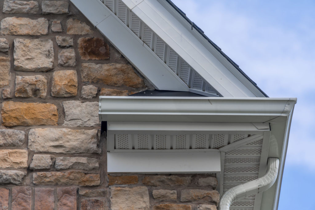 View from below of stone-sided home with installed gutters and gutter guards.