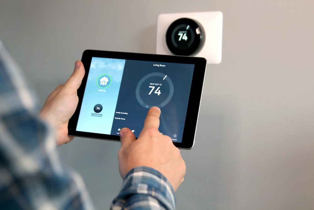 Homeowner using a tablet with smart home app in front of thermostat.