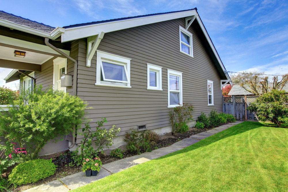 The side of a brown home with white windows.