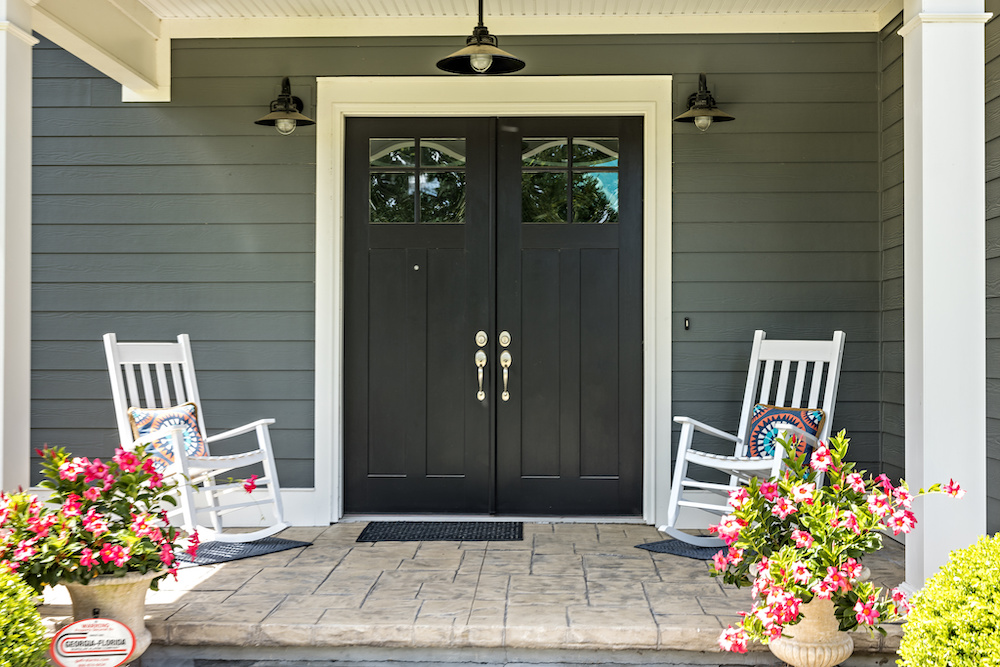 A front porch with two rocking chairs, stamped concrete floors, and double doors.